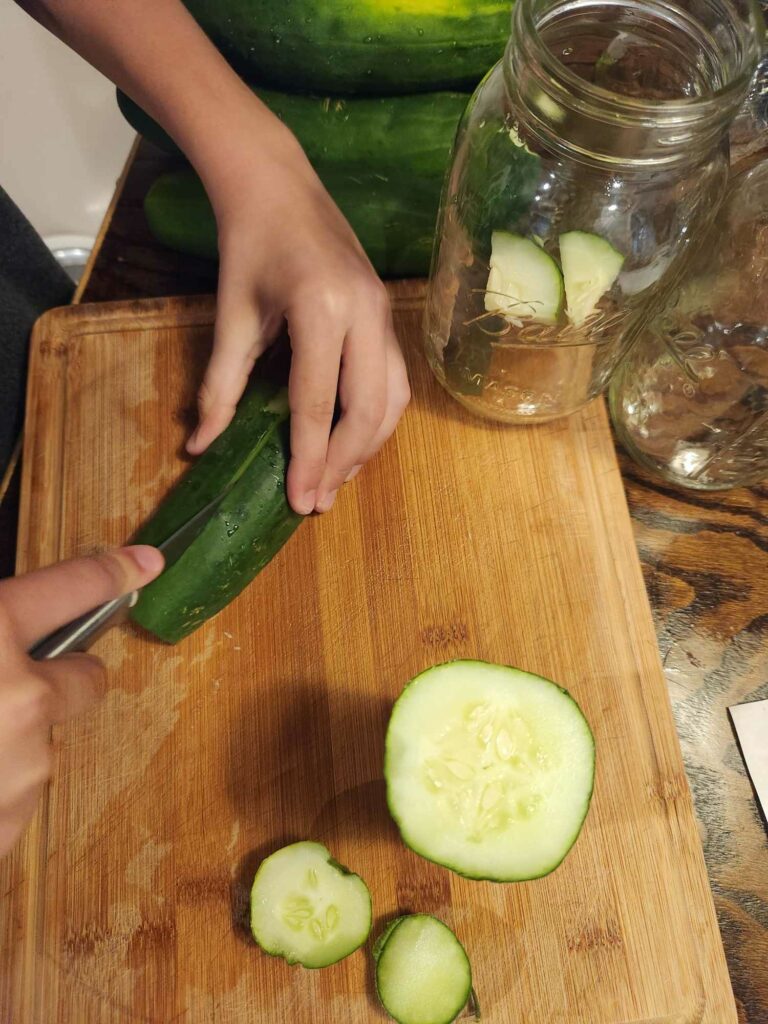 slicing cucumbers on cutting board, placing pickles in mason jar